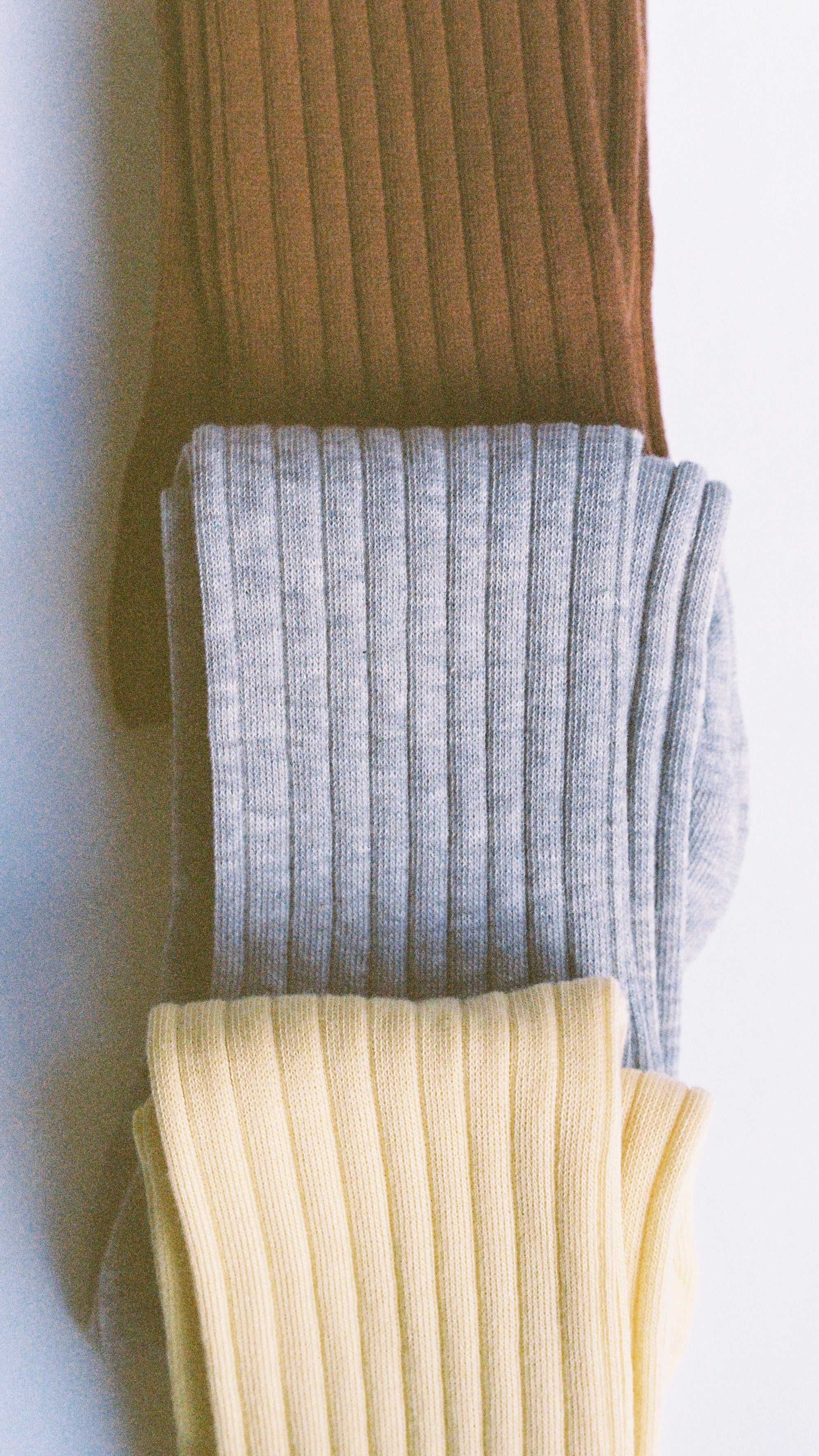 Three pairs of ribbed socks in brown, gray, and yellow on a white background