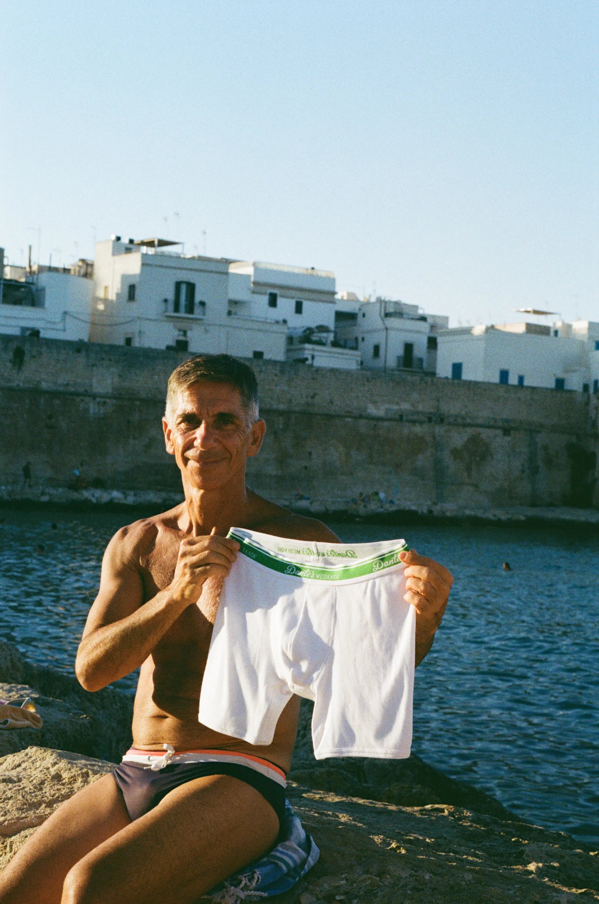 Man holding a pair of white boxer briefs in Monopoli, Puglia at the beach.